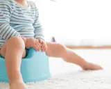 Dziecko w pasiastej bluzce siedzi na niebieskim nocniku, rozpoczynając naukę czystości.