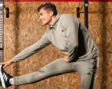 Ein Mann in Trainingskleidung macht dynamisches Dehnen vor einer Holzwand.