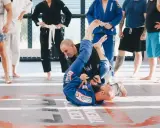 Dwóch mężczyzn w niebieskich kimonach ćwiczy chwyty na macie. To właśnie bjj co to za sztuka walki, która uczy kontroli i poddań.