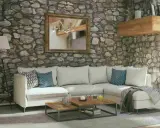 Soggiorno accogliente con pareti in pietra grezza, divano bianco, tavolini in legno e specchio dorato. Ottime idee pareti in pietra per un ambiente rustico.