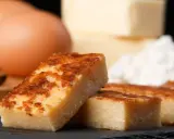 Porciones doradas de quesada, con huevos y harina al fondo. Ingredientes para una deliciosa receta quesada.