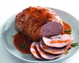 Un succulento arrosto di manzo, affettato e nappato con salsa, servito su un piatto con rosmarino.