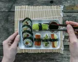 En bricka med olika sorters sushi, perfekt för ett enkelt sushi recept. En hand håller ätpinnar redo att plocka upp en bit.