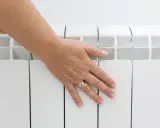 Main posée sur un radiateur électrique blanc, vérifiant la température hors gel.