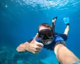En man snorklar och ger tummen upp i det klara vattnet vid Nerja strand.
