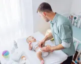 Ojciec zmienia pieluszkę dziecku na przewijaku.