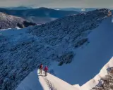 Två vandrare på en snöig bergskam med utsikt över fjällandskap. Detta är Sveriges högsta berg.
