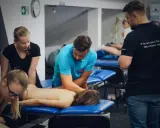 Uczestnicy szkolenia doskonalą technikę masażu tkanek głębokich, pracując nad plecami pacjenta.