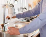 Persona llena un vaso de agua de un grifo con filtro. ¡Qué alivio, no tengo agua en casa y esto me salva!