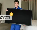 Hombre sonriente sostiene un televisor, listo para instalarlo. La altura ideal para un mueble de TV suspendido es clave.