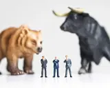 Miniature businessmen stand between a bear and a bull, symbolizing market volatility and the quest for art investment returns.