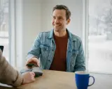 Uśmiechnięty mężczyzna płaci telefonem w Szwecji. Choć nie można tam płacić euro, transakcja przebiega sprawnie.