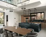 Nowoczesny salon z kuchnią otwartą: drewniane meble, czarna wyspa kuchenna, designerskie lampy i duży stół jadalniany.
