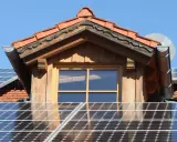 Dach mit Solarmodulen, die erneuerbare Energie von der Sonne einfangen. Ein Fenster und ein Dachüberstand aus Holz sind sichtbar.