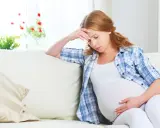 Zmęczona kobieta w ciąży, 26 tydzień, który miesiąc? Siedzi na kanapie, trzymając się za głowę.