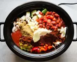 En slow cooker fylld med hackade grönsaker, tomater och kryddor, redo att bli en smakrik gryta.
