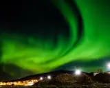 Spektakularna zorza polarna rozświetla nocne niebo nad ośnieżonymi wzgórzami i światłami miasteczka. To idealny moment, kiedy występuje zorza polarna.