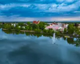 Widok na jezioro z fontanną i zabudowaniami, w tym kościołem. Odkryj iława atrakcje, które zachwycają o każdej porze dnia.