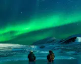 Två personer sitter på isen och ser på det magiska noorderlicht zweden. Snöklädda berg och stjärnor lyser upp natten.
