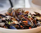 Un plato rebosante de mejillones al vapor, con sus conchas abiertas mostrando la carne anaranjada y jugosa.
