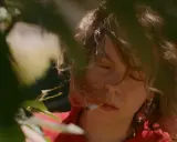 En närbild på Nina Widerberg med en cigarett i munnen, omgiven av gröna blad.
