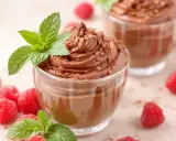 Délicieuse mousse au chocolat 2 ingrédients sans oeuf, garnie de copeaux de chocolat et de menthe fraîche, avec des framboises autour.