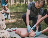 Uczestnicy kursu przetrwania ćwiczą resuscytację na fantomie w lesie.