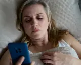Kobieta leży w łóżku, trzymając telefon. Może to być związane z problemem oddawania moczu w nocy jeden raz.