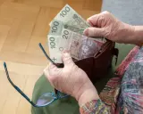 Dłonie starszej osoby wyciągają pieniądze z portfela. Widać banknoty 100 zł i 20 zł, być może to oczekiwana trzynasta emerytura.