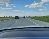 Jadąc na S7, widzimy pola i chmury. Samochody poruszają się po pustej drodze.
