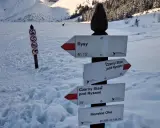 Znak szlaku w Tatrach wskazuje drogę na Rysy. W tle zamarznięte Morskie Oko i ośnieżone szczyty.