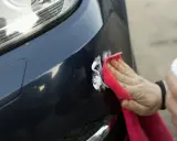 Ręka z czerwoną mikrofibrą poleruje drobne rysy na ciemnym lakierze auta, przywracając blask dzięki ceramice.