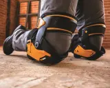 Protection des genoux pour éviter toute maladie professionnelle. Des genouillères robustes et orange protègent les genoux d'un travailleur sur un sol poussiéreux.