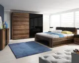 Dormitorio con muebles oscuros de madera y cristal negro. Pared azul oscuro, alfombra azul y cama con ropa de cama blanca y azul.