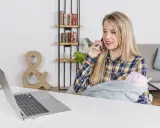 Kobieta z dzieckiem na rękach rozmawia przez telefon, pracując przy laptopie. To przykład pracy z orzeczeniem o niepełnosprawności, pokazujący elastyczność i możliwości.