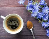 Taza de café de achicoria, con flores azules y una cucharada de polvo de achicoria, ideal para aprender como preparar achicoria en cafetera.