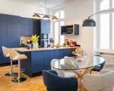 Élégante petite cuisine ouverte avec îlot central bleu marine, tabourets en bois et table en verre.