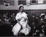 Una mujer con corona de flores baila en una celebración, rodeada de gente. Podría ser una boda gitana.