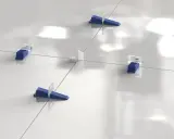 Sistema de nivelación de baldosas con cuñas azules y separadores blancos. La **matajunta desplazada** asegura una instalación perfecta.