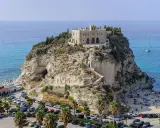 Santuario di Santa Maria dell'Isola a Tropea, regione Calabria, su uno sperone roccioso a picco sul mare azzurro, con spiaggia e palme.