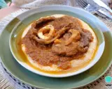 Un plato de osobuco de ternera cocinado a fuego lento, servido sobre una cama cremosa de polenta.