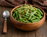 Salade haricots verts croquants, parsemée de graines de sésame et de petits morceaux croustillants. Une cuillère en bois est à côté du bol.