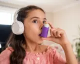 Mädchen mit Kopfhörern benutzt Inhalator gegen Asthma durch Stress.