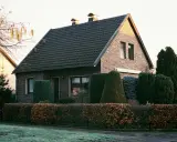 Ein gepflegtes Einfamilienhaus mit Ziegelfassade und dunklem Dach. Die Frage "wie viel kostet ein haus" wird durch die idyllische Szenerie aufgeworfen.