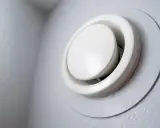 Grille de ventilation blanche, ronde et réglable, fixée sur un mur gris. Un système vmr hygroréglable pour une meilleure qualité de l'air.