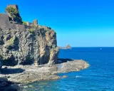 Castello Normanno a Aci Trezza, un luogo da vedere. Roccioso promontorio sul mare blu, con un antico castello in pietra e vegetazione.