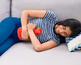 Joven con bolsa de agua caliente en el abdomen, aliviando el dolor de cólicos.