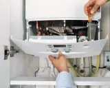 Hände reparieren einen Thermoflow Durchlauferhitzer. Eine Anleitung wird befolgt, um die Komponenten zu überprüfen.