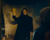 En man i svart rock håller upp en gul skalle framför en målning. Kanske en scen från skurkarnas skurk film.