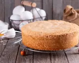 Puszysty biszkopt z olejem, obok jajka i trzepaczka, gotowy do dekoracji.